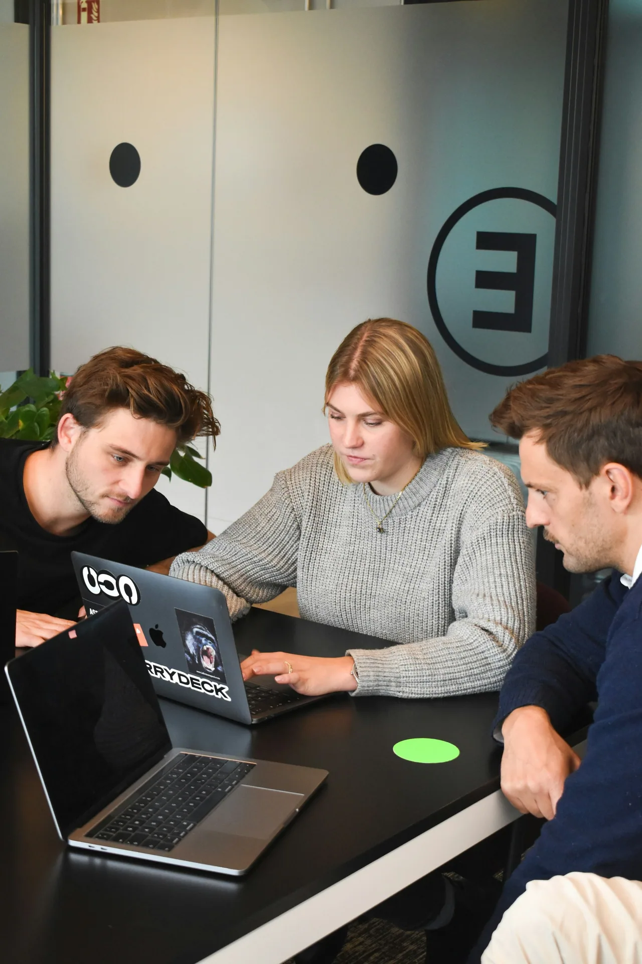 Three people collaborating around a laptop in an office
