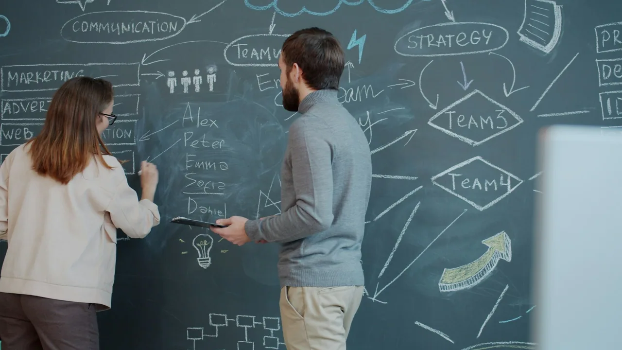 Two people planning beside a chalkboard in an office